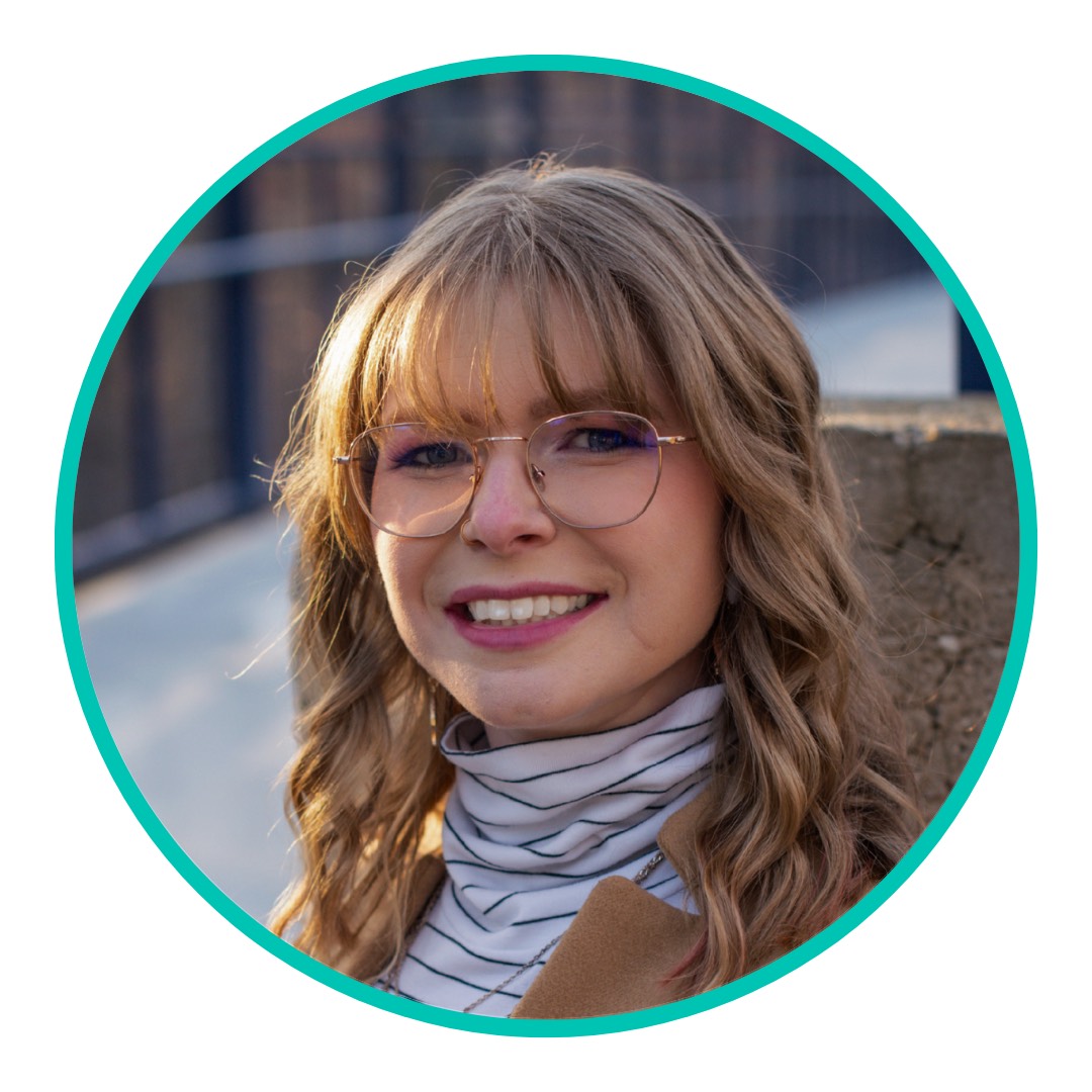 A white woman with blonde hair and glasses wearing a striped turtleneck and blazer